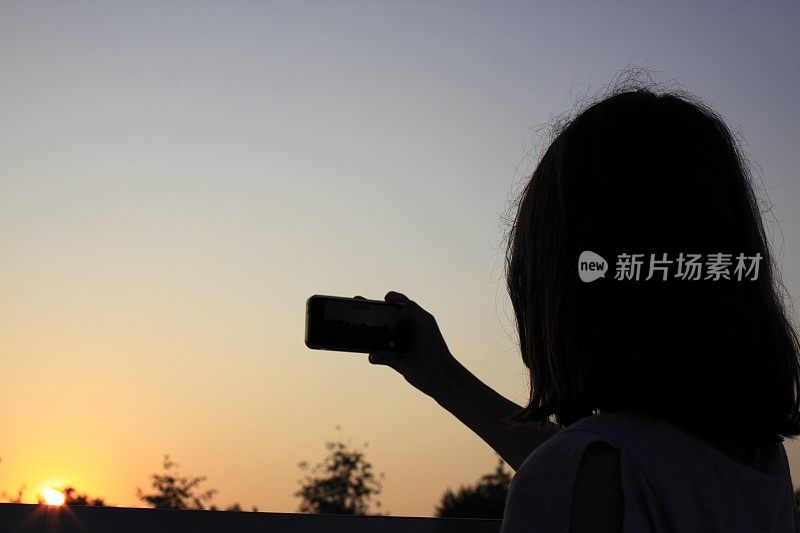 一个拿着手机的小女孩的剪影。少年在夕阳下用手机自拍。一个女孩用一个装置拍下了夜空的照片。