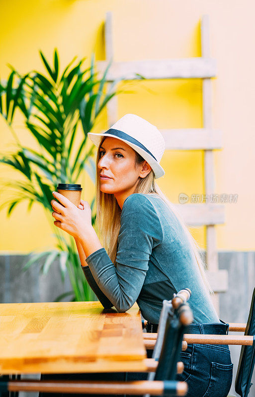 漂亮的金发女人用纸杯喝咖啡