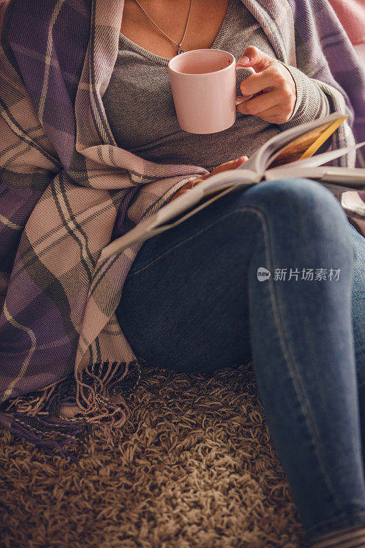 一个面目全非的年轻女子，一边喝着咖啡，一边读着书