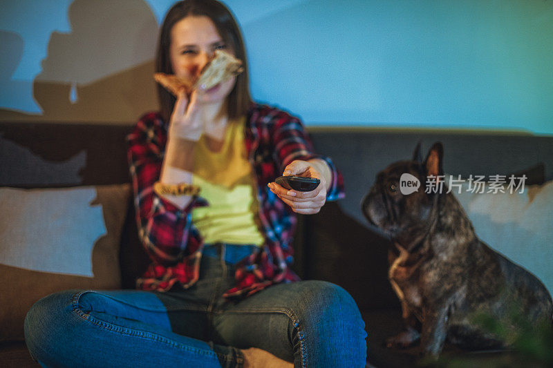 一个女人在沙发上吃披萨，和她的狗一起看电视