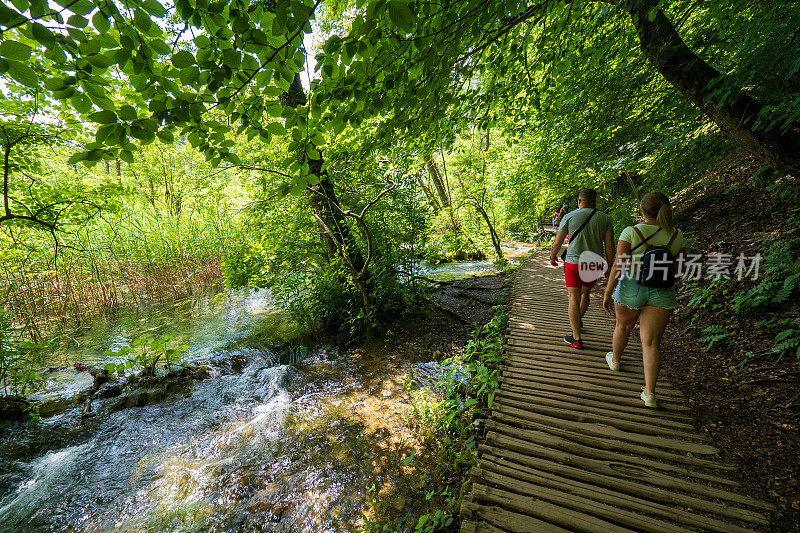 克罗地亚Plitvice湖国家公园，徒步者沿着木制人行道散步，穿过瀑布，冲向隐藏的池塘