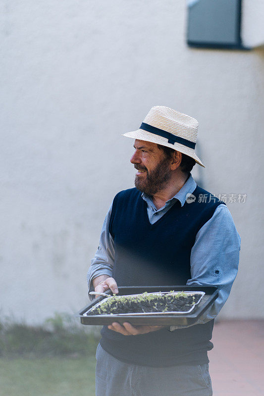 一个成熟的男人在花园里捧着一盘秧苗