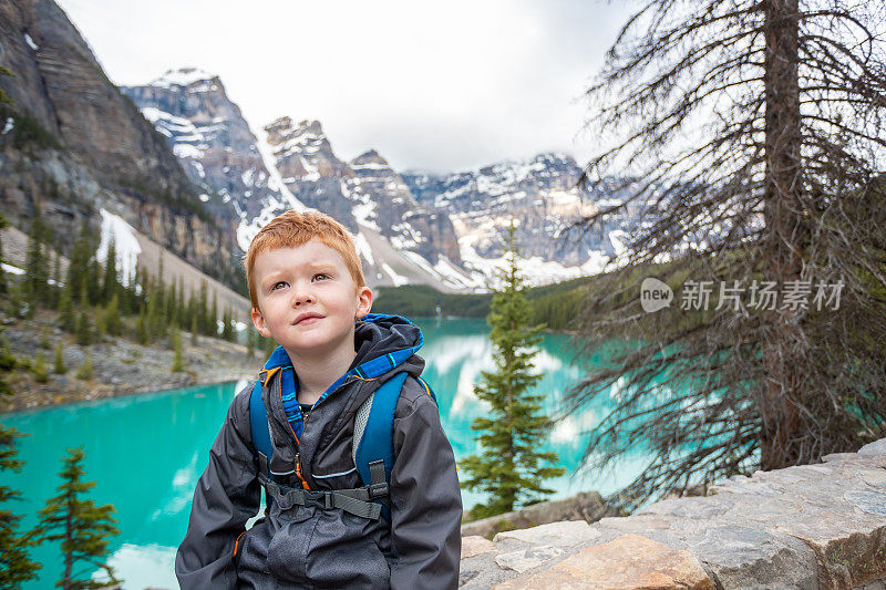 快乐年轻可爱的红发男孩坐在夏天的冰碛湖