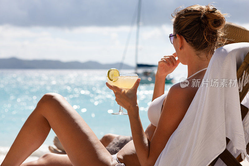 一对夫妇在热带海滩的柚木躺椅上喝着鸡尾酒放松