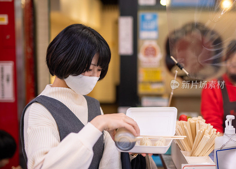 一名年轻女子戴着保护面罩，在街上的馒头上涂酱油