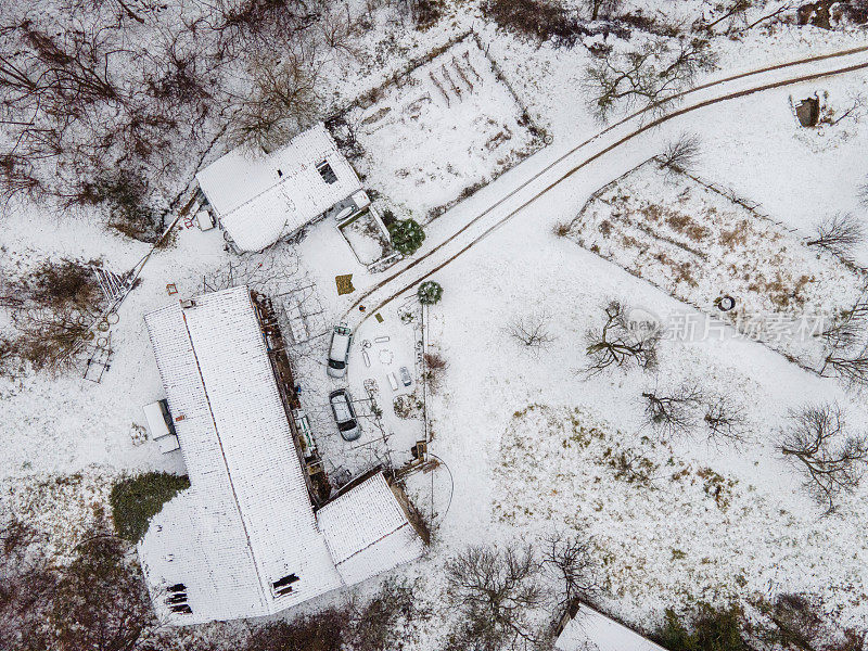 正上方两辆车停在一所房子前面，乡间景色覆盖着雪