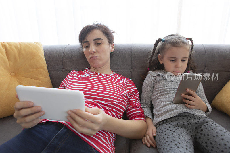妈妈和小女儿一起使用平板电脑和智能手机放松