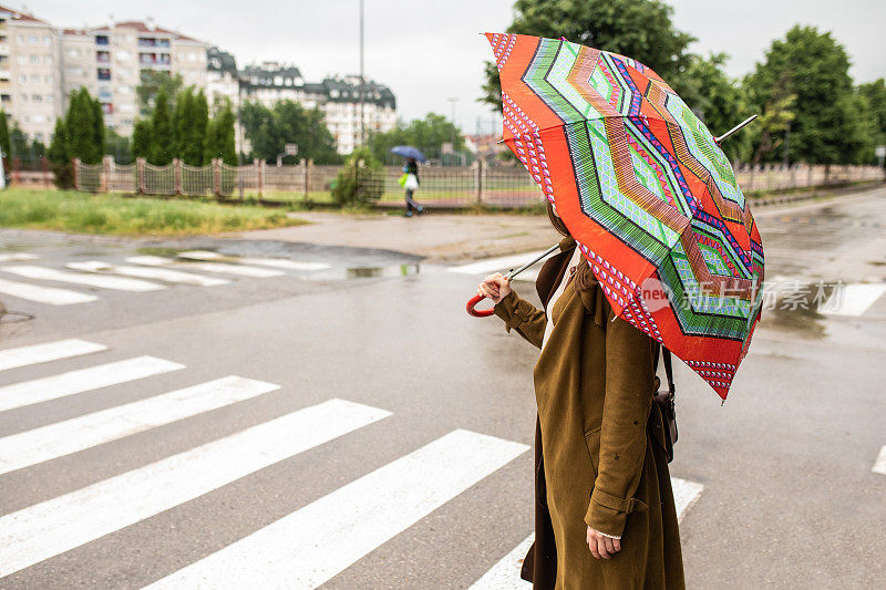 女性行人撑着雨伞在雨天过马路