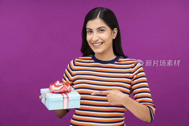 一个年轻女人的肖像展示和拿着礼品盒孤立地站在紫色的背景