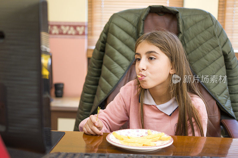 漂亮的女孩一边用电脑一边吃炸土豆