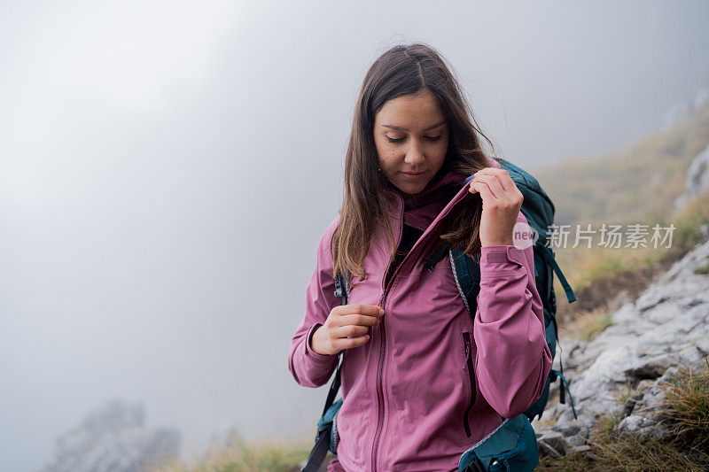 一名女徒步旅行者拉上雨衣的拉链，因为雾滚滚而来