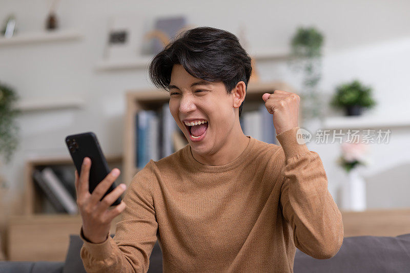 一名亚洲男子在手机屏幕上微笑着表达他的快乐。他得到了好消息，露出了高兴的样子。技术可以帮助我们有更方便的连接