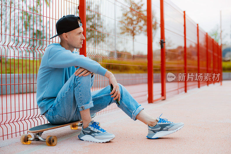 年轻的潮男滑板自拍与手机，而坐在滑板户外
