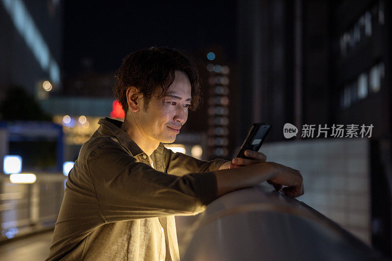 夜间行人天桥上使用智能手机的男子的侧视图——微笑