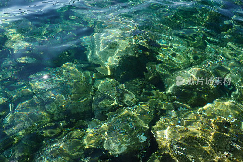 碧蓝碧蓝透明的海水海水质感。水面和波纹的俯视图。水海浪背景。透过清澈的海水，可以看到布满藻类的岩石底部