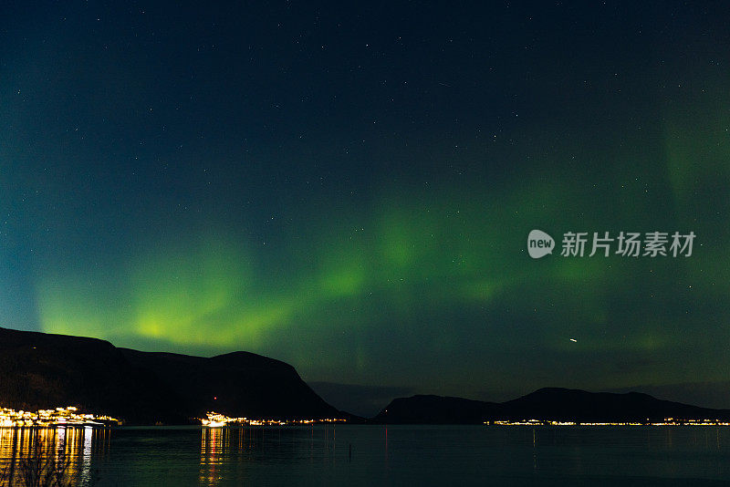 风景秀丽的北极光在峡湾和发光的城镇在挪威