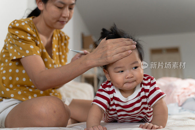 年轻的亚洲母亲照顾和使用数字体温计和手检查体温她的儿子在疾病期间流感发烧。家庭宝宝生活方式照顾和保健理念。