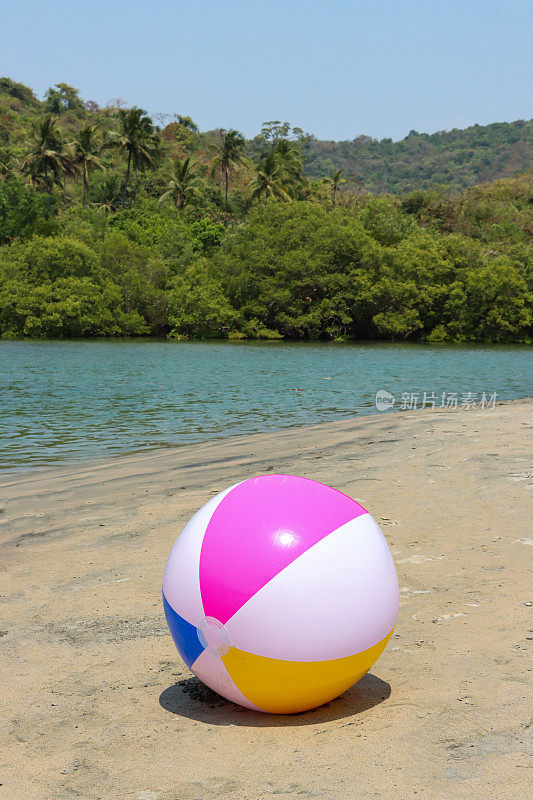 在泻湖沙滩上的沙滩球图像，塑料，色彩鲜艳的儿童沙滩玩具，海洋和林地背景，重点在前景