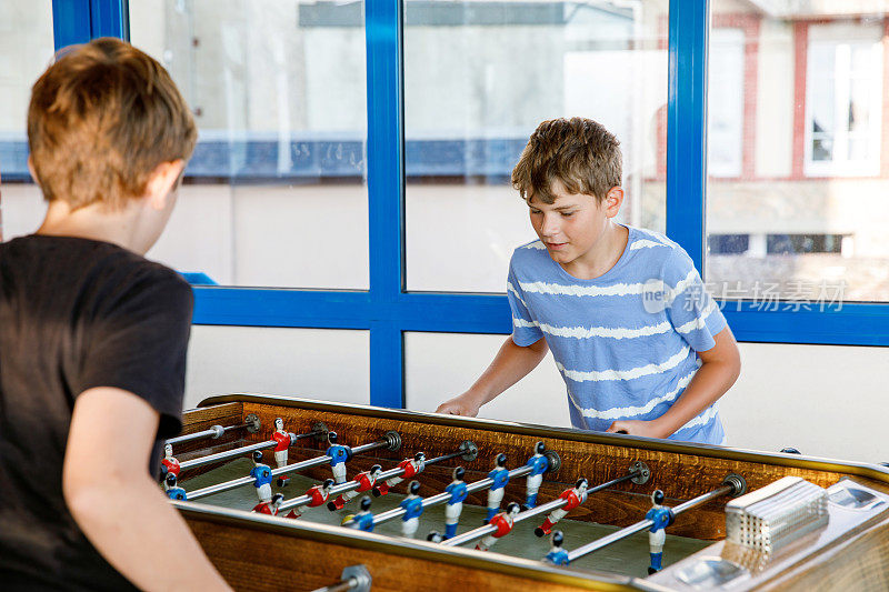 两个面带微笑的男生在玩桌上足球。快乐兴奋的孩子与兄弟姐妹或朋友玩家庭游戏的乐趣。积极的青春期前的孩子或青少年。
