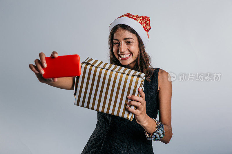 老练而优雅，一个穿着讲究的女人站在工作室里，抱着精心包装的礼物自拍，她的眼睛里充满了兴奋，因为她欢迎假期
