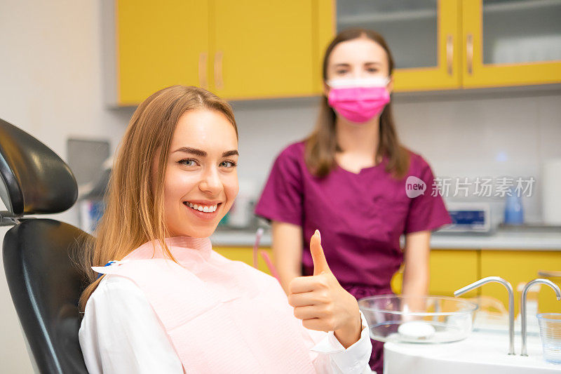 在牙科诊所，年轻的女病人竖起大拇指坐在医疗椅上