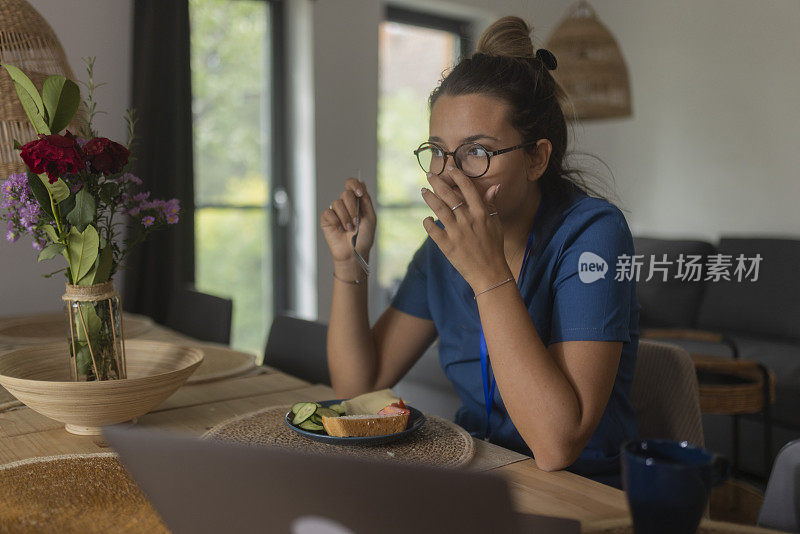 穿着制服的医疗技术人员在上班前在家吃早餐，坐在餐桌前使用笔记本电脑