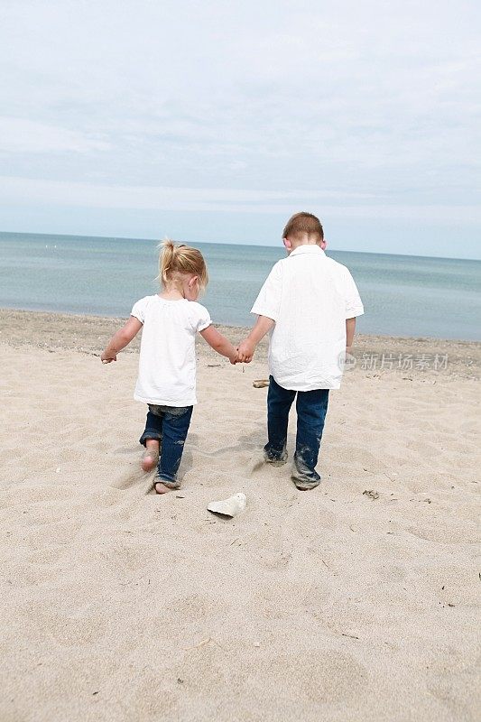 小孩子手牵着手在海滩上散步