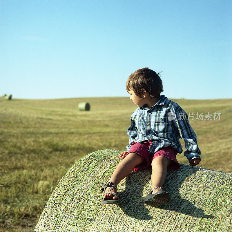 在午后的阳光下，一个农家男孩坐在干草捆上