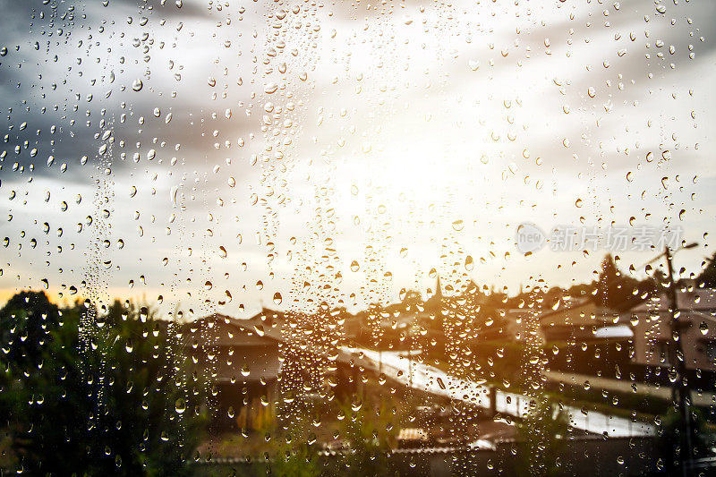 在一个阴雨天，阳光出现在焦点不清的背景下，水珠滴在玻璃窗户上的特写画面