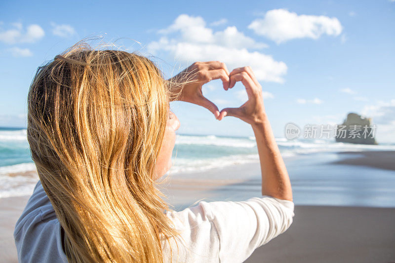 年轻女子在海滩上做心形指架