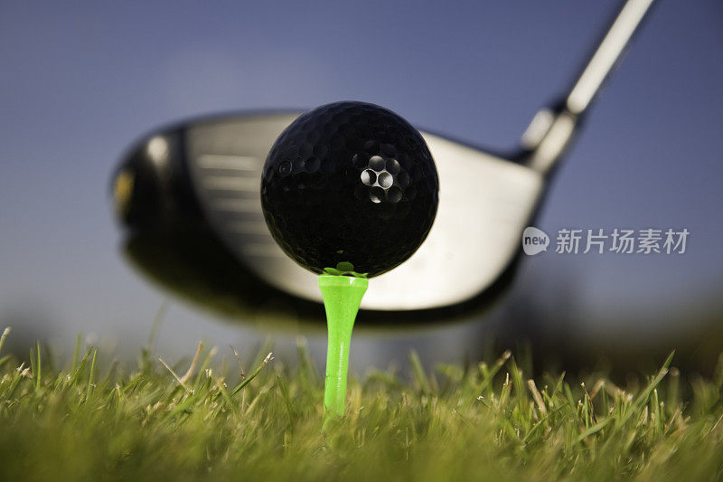 黑色高尔夫球，位于球杆前方的绿色球座上