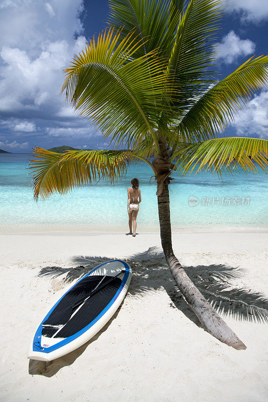 一名女子从加勒比海海滩上的冲浪板上走出来