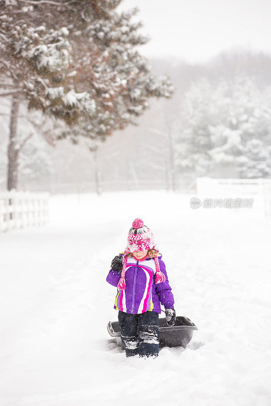 年轻的女孩走在冬天的暴风雪拉雪橇