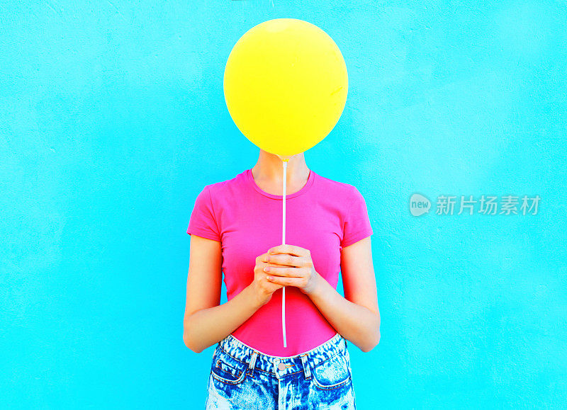 Ð多彩的女人隐藏着脸黄色的气球在蓝色的背景上玩