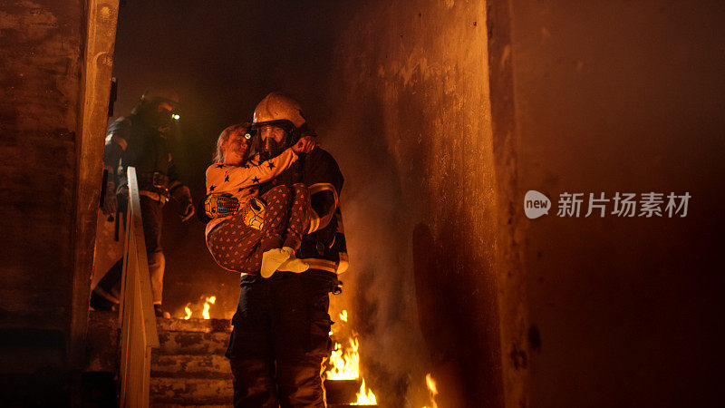 勇敢的消防员抱着一个被救下的女孩走下燃烧的大楼的楼梯。