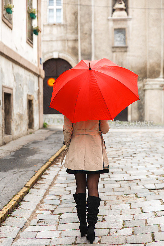 拿着红伞的女人走在旧城里。