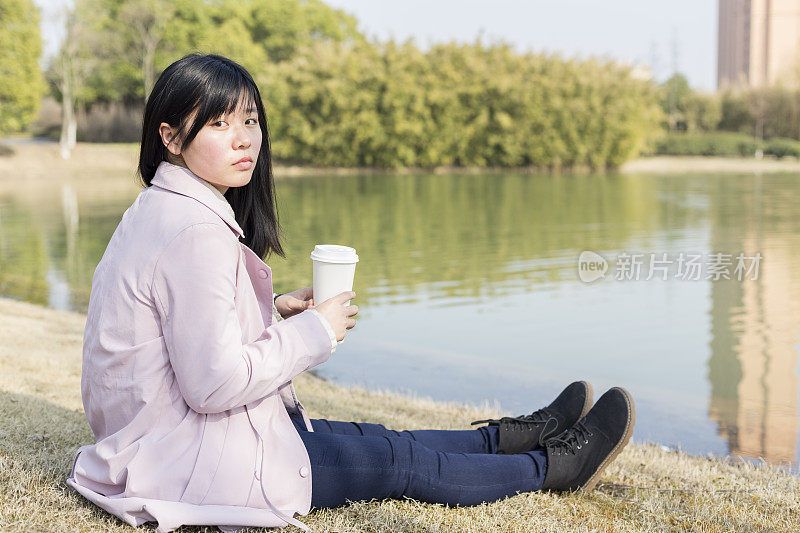 年轻女性拿着一次性杯子在草坪上
