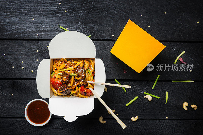 乌冬炒面条与肉和蔬菜在一个盒子在黑色的背景。用筷子和酱汁。