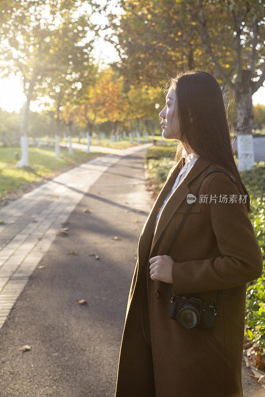 年轻女子拿着相机走在公园小径上