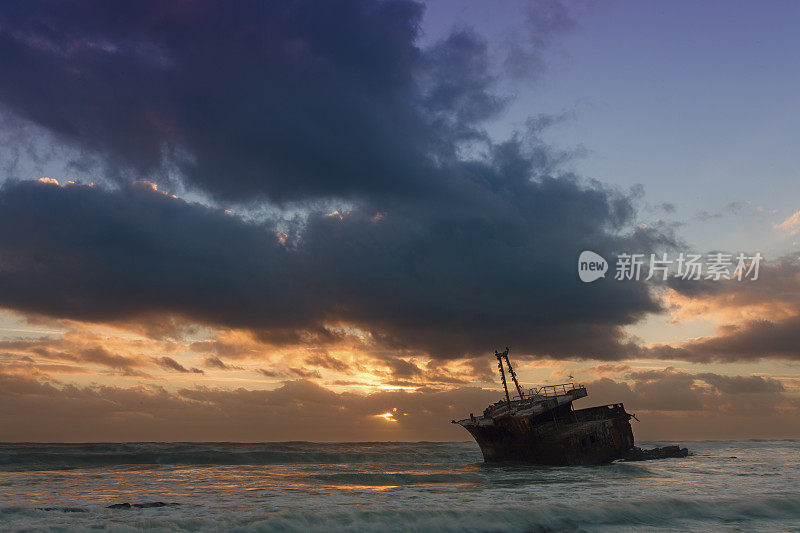 日落时，一艘老船的残骸长时间暴露在岩石上