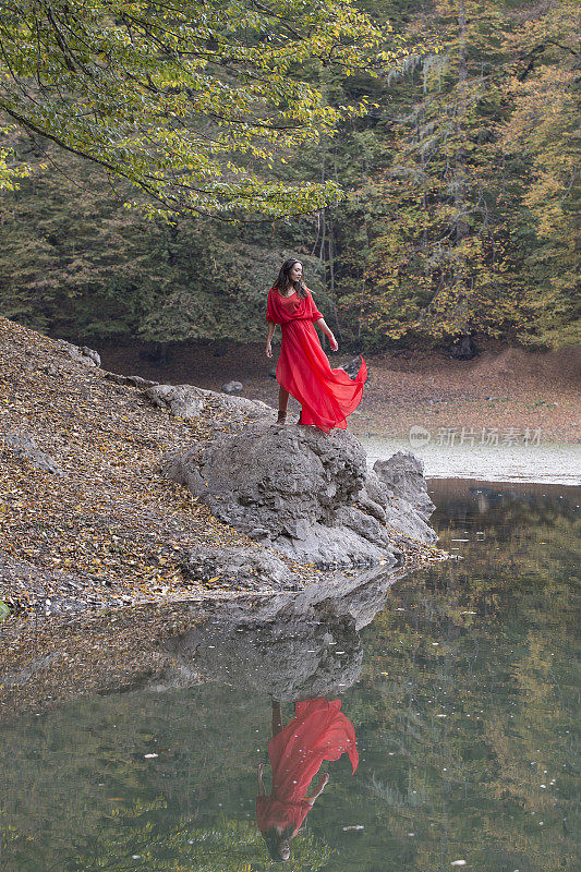 秋天森林里的女孩。湖中童话般的倒影。时尚的女人站在公园的湖边