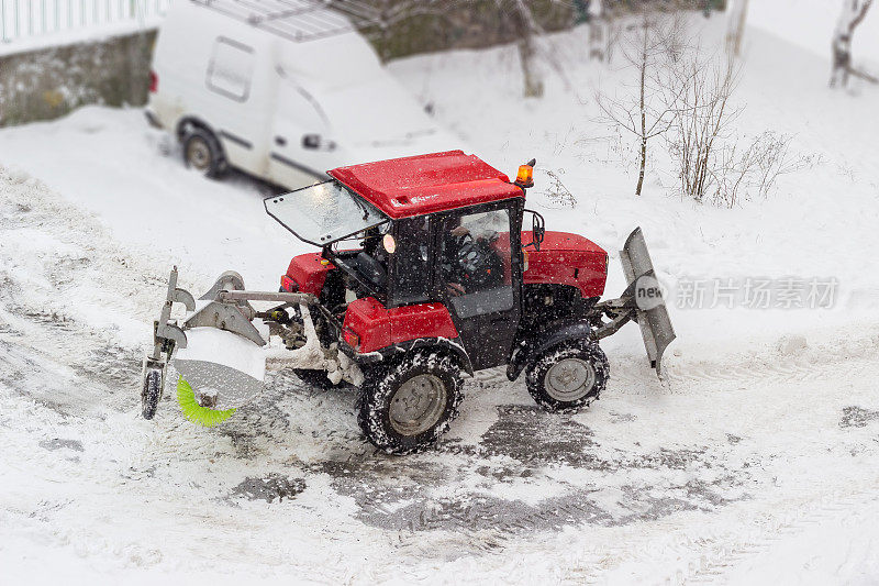 小型红色拖拉机在下雪时在院子里扫雪机