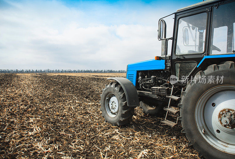 一辆旧的蓝色拖拉机停在空旷的田野里。农业机械，田间工作。