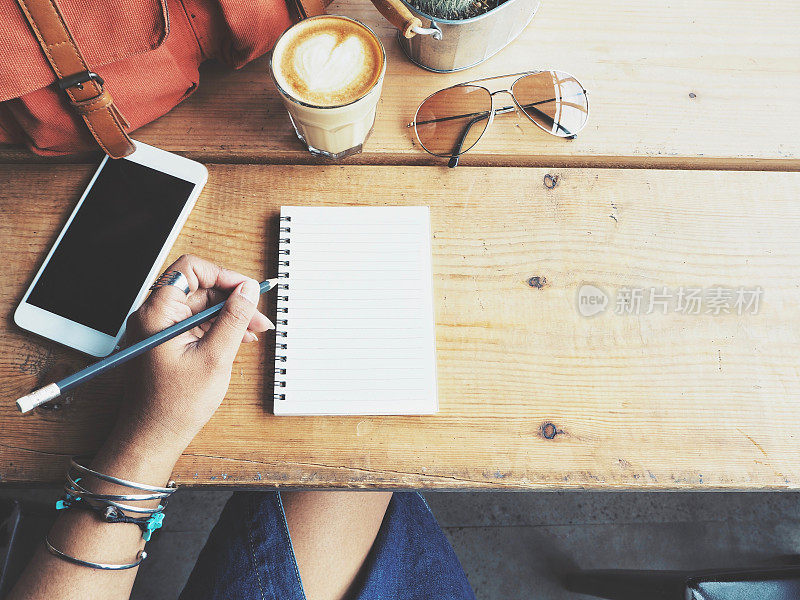 女人拿着笔在纸上写字，咖啡杯在办公桌上放着智能手机