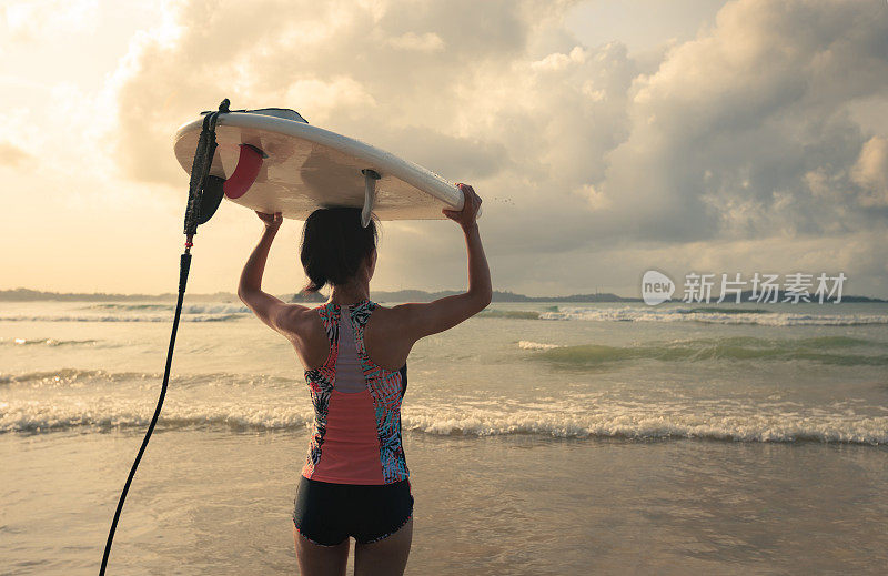 后视图的年轻女子冲浪者与白色冲浪板走到海边