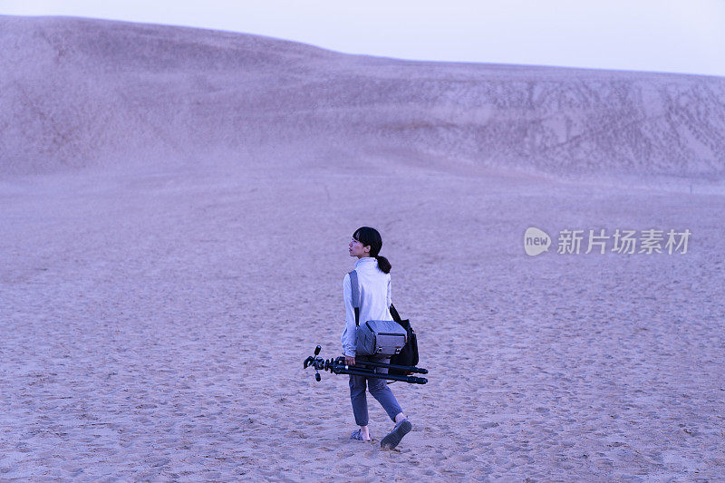 女摄影师在黎明的沙漠中行走