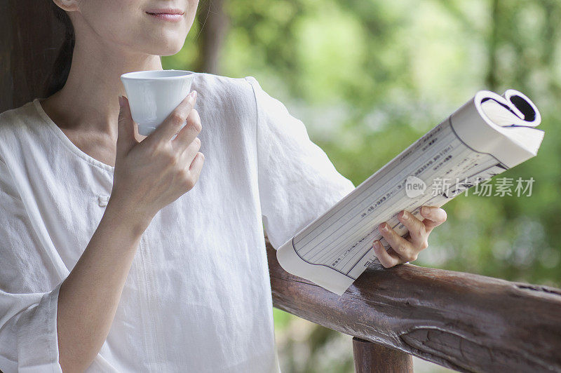 年轻女人拿着古书边喝茶