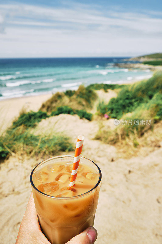 在一个炎热阳光明媚的夏日，手拿一杯冰白咖啡在纽基的菲斯特拉海滩。