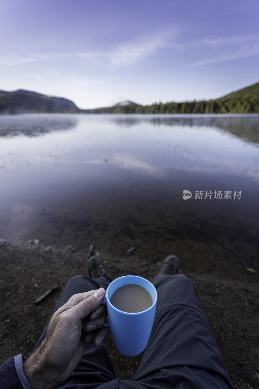 在秋天露营的湖边喝咖啡的男人