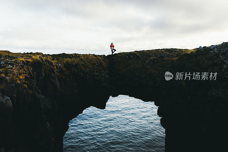 在冰岛，一个女人在美丽的拱门上做瑜伽，看着大海